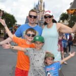 A smiling family stand in front of the magic family with their hands up. There are two adults and three boys.