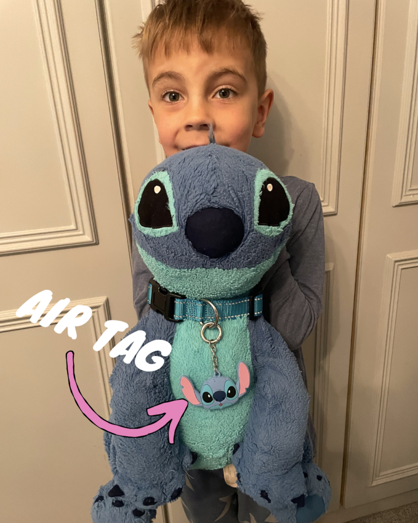 Little boy holding a precious Stitch stuffy with a dog collar on and airtag round its neck.