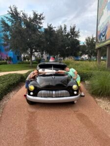 Picture showing my two youngest boys trying to hold hands ver the bonnet of a large model of a cartoon car from the cars film whilst on a trip to the Art of Animation resort