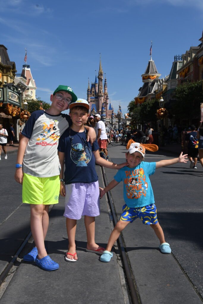 Three boys stand smiling in front of the castle at Walt Disney World