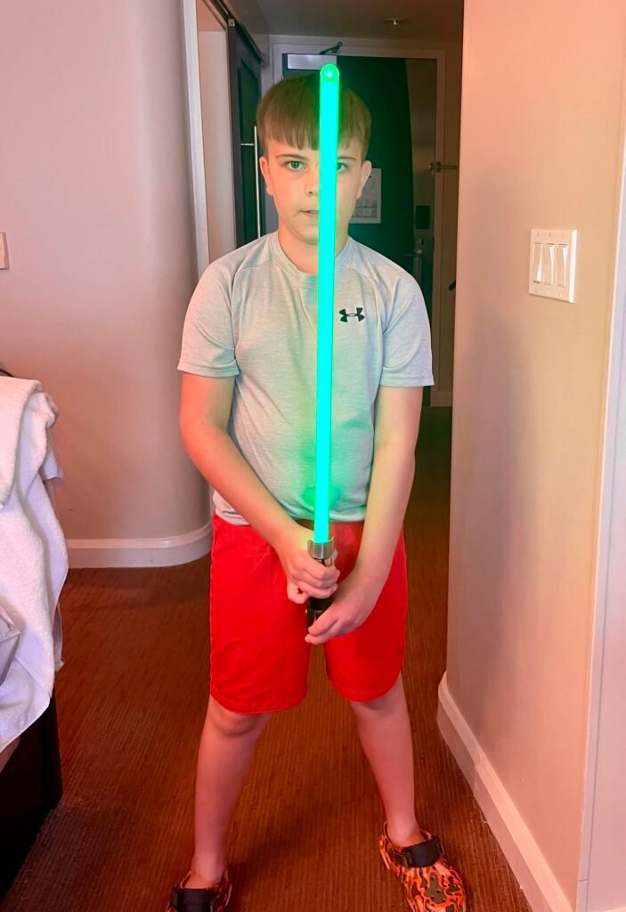 A boy or around 10 years old holds a green light saver in front of him in a hotel room - The Hidden costs of a Disney Holiday
